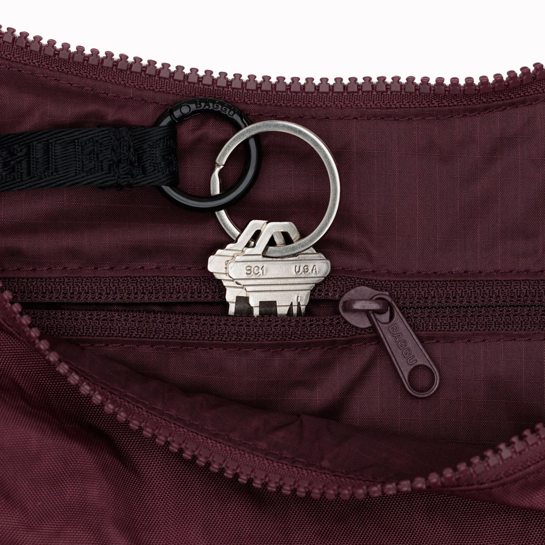 The Medium Crescent Bag in Mahogany from Baggu is a stylish and versatile accessory that can complement any outfit. It is made of durable nylon and features a zippered main compartment, an interior slip pocket, and an adjustable shoulder strap.