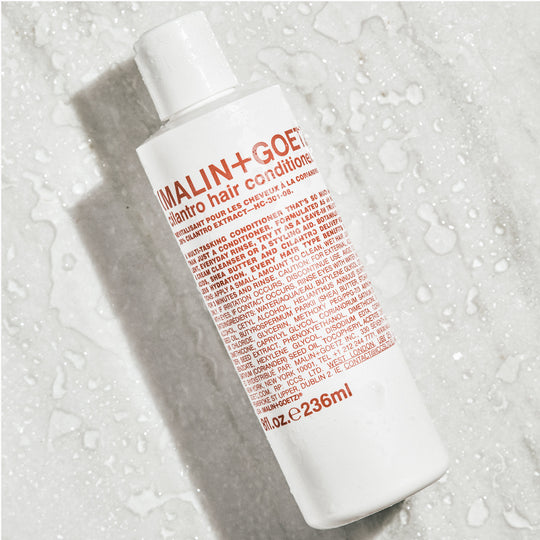 Cilantro (Coriander) Hair Conditioner from Malin+Goetz is a lightweight, multi-purpose hair conditioner that hydrates all hair and scalp types and forms part of Malin+Goetz's essentials collection. Bottle shown here on a wet background.