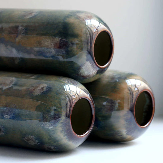 The deep green hued Marshland design is hand-thrown in watertight stoneware and due to the rounded taper at the top of the vase, the glaze melts down the sides of the cylindrical vase mimicking melting ice.