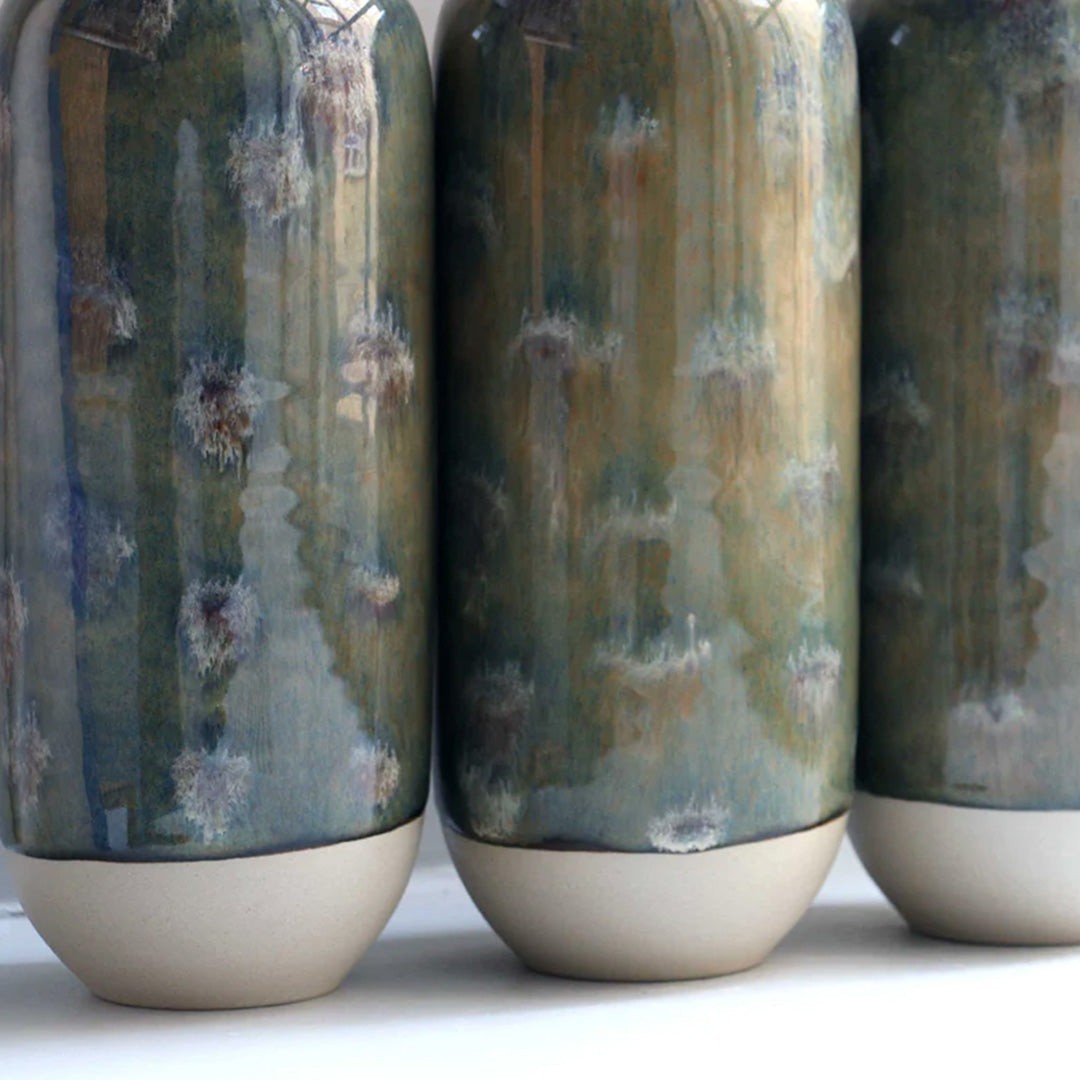 The deep green hued Marshland design is hand-thrown in watertight stoneware and due to the rounded taper at the top of the vase, the glaze melts down the sides of the cylindrical vase mimicking melting ice.