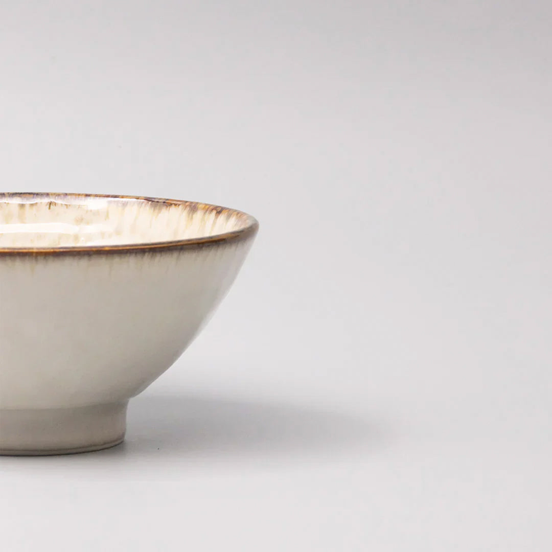 A handcrafted ceramic bowl with a gently flared profile, featuring a creamy glaze with warm, toasted rim accents.