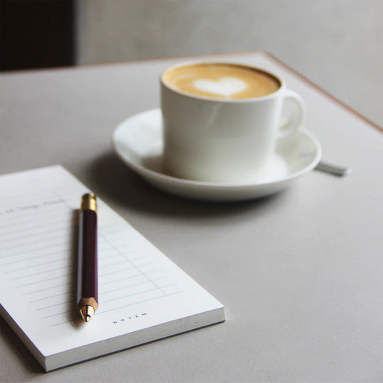 Milo To-Do List with coffee on table. The book has 56 pages of undated weekly spreads, while the notepad has 60 sheets of weekly planner sheets. Both formats have a horizontal layout with space for notes and must-do's of the week.