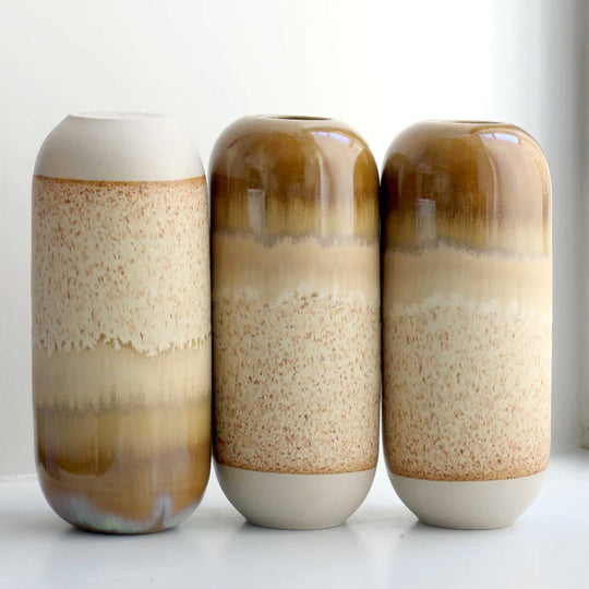 The brown hued Mirrored Earth design is hand-thrown in watertight stoneware and due to the rounded taper at the top of the vase, the glaze melts down the sides of the cylindrical vase mimicking melting ice.