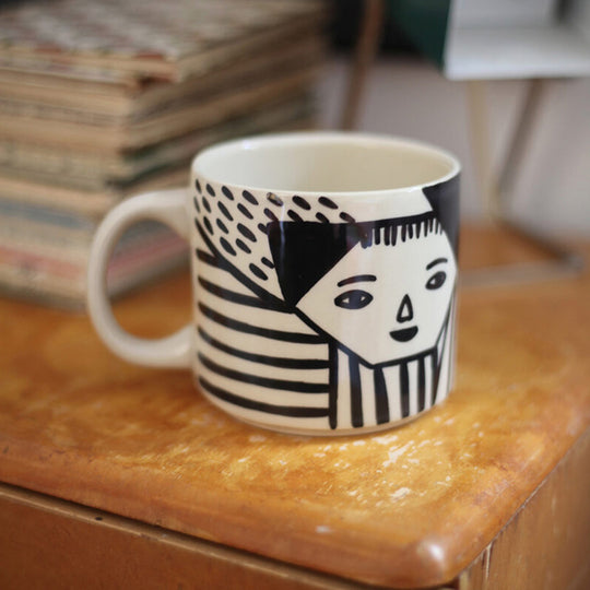 Donna Wilson mug featuring an illustrated black and white face nestled amongst abstract patterns. Every mug is painted by hand, meaning each one is unique.  100% stoneware.