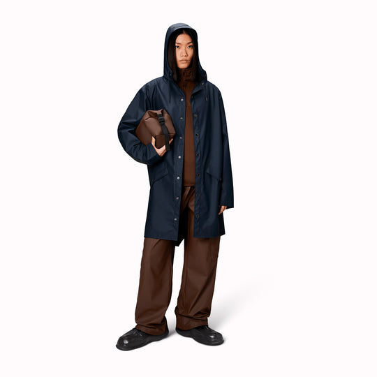 An ever-contemporary unisex rain jacket from Danish Outerwear and Lifestyle company Rains. This long Navy Blue rain jacket is characterized by a minimal silhouette in a long design.