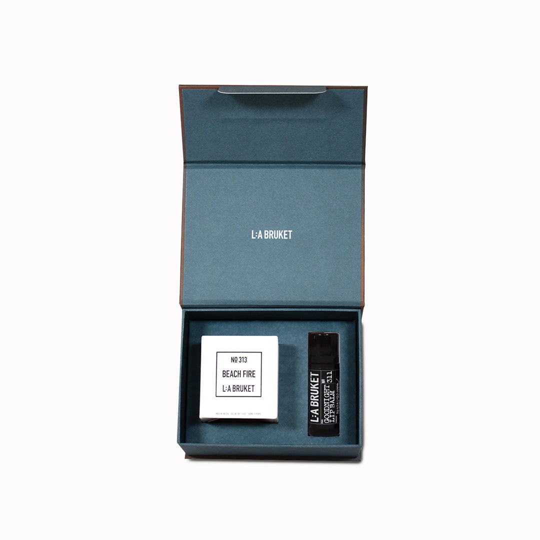 The L:A Bruket 2025 Nightfall Winter Gift Kit contains a soothing duo to wind down the day and prepare for a good night of sleep: 313 Candle Beach Fire 50g and 311 Goodnight Orange Blossom Lip Balm 14g