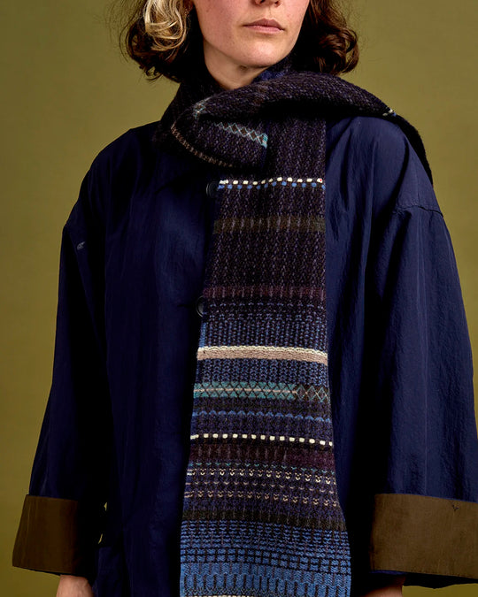 The Noah scarf features a subtle textured weave of background colour offset by intricate detailing at the borders, where delicate floral motifs and patterns mingle with bold cross-hatches, contrasting pinstripes, and graphic bands.&nbsp;