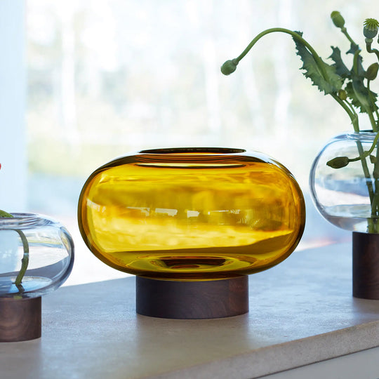 A flattened spherical mouth blown Amber glass vessel sits on a Walnut wood base. This is a beautiful and versatile piece, suitable for use as a vase, or as a candle lantern