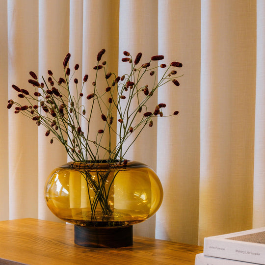 A flattened spherical mouth blown Amber glass vessel sits on a Walnut wood base. This is a beautiful and versatile piece, suitable for use as a vase, or as a candle lantern