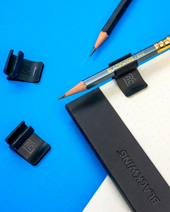 The Blackwing Pencil Holder is a simple metal clip designed to attach securely to the cover of your favourite notebook, giving your pencil a dedicated place to live.