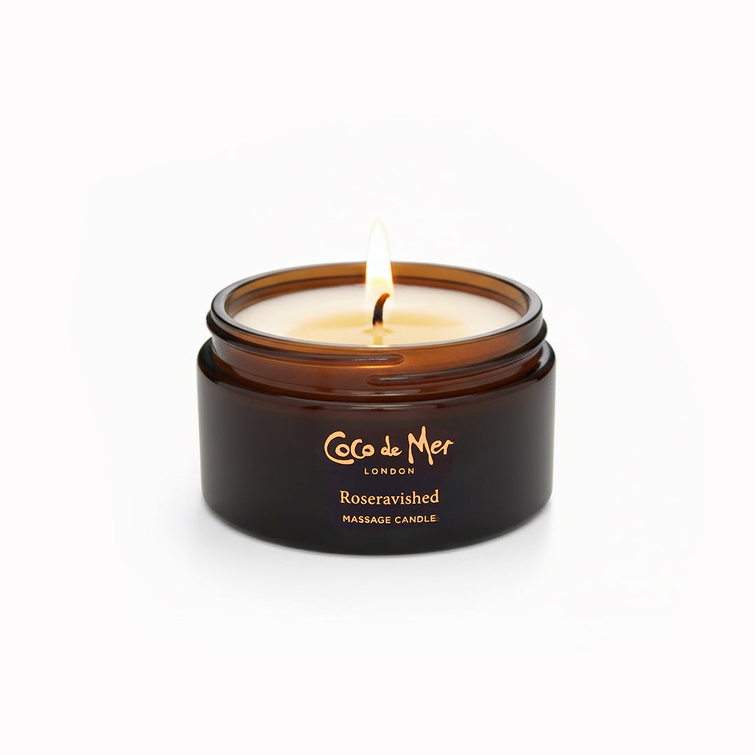 Coco de Mer London massage candle with a lit wick on a white background