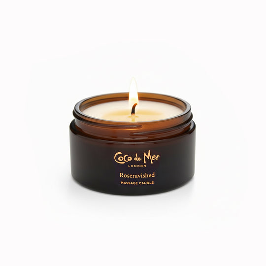 Coco de Mer London massage candle with a lit wick on a white background