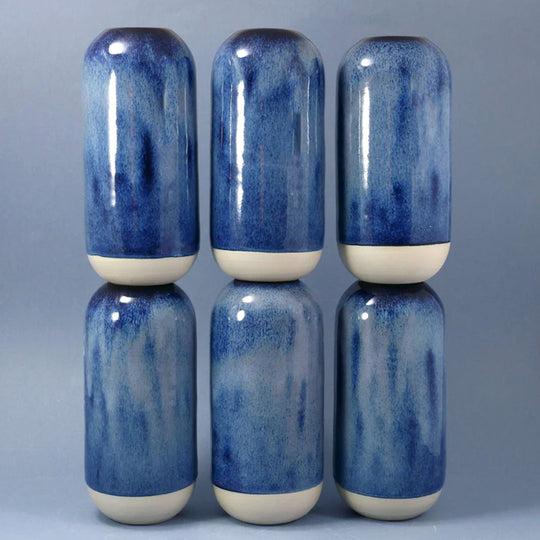 The deep blue hued Shadow Blue design is hand-thrown in watertight stoneware and due to the rounded taper at the top of the vase, the glaze melts down the sides of the cylindrical vase mimicking melting ice.