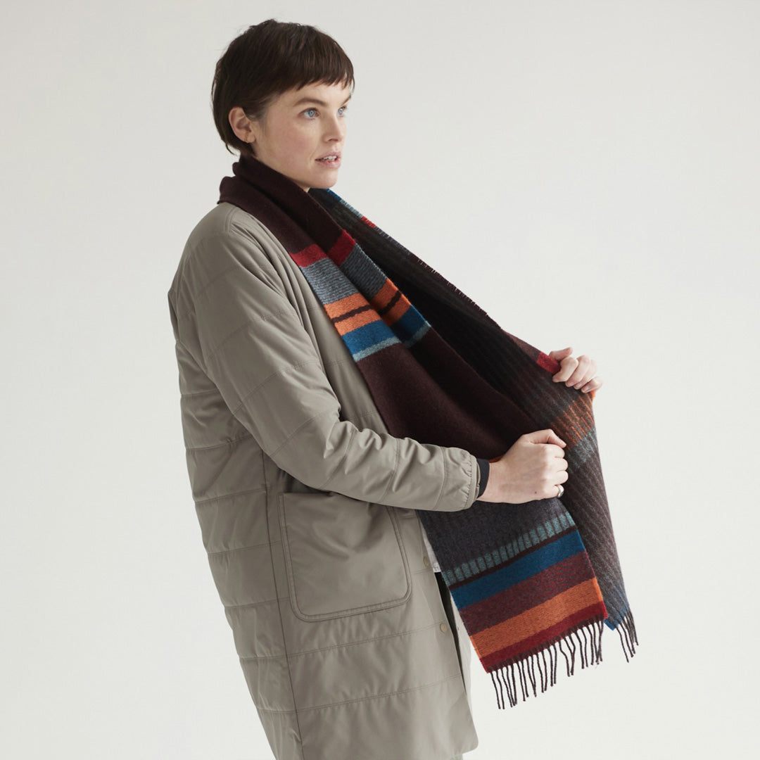 As Worn - The Strathay Cinder Lambswool scarf by Wallace and Sewell is a 100% Merino Lambswool scarf displaying a deep peat palette and berry red tones to add warmth, while the burst of orange adds a lively touch.