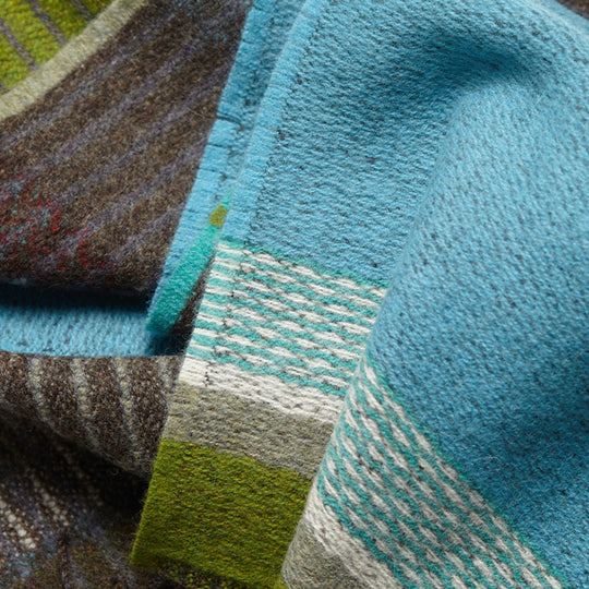 The Strathay Verdigris Lambswool scarf by Wallace and Sewell is a 100% Merino Lambswool scarf in a colourful pattern of verdigris blue, moss and orchard green, with a pop of dark red.