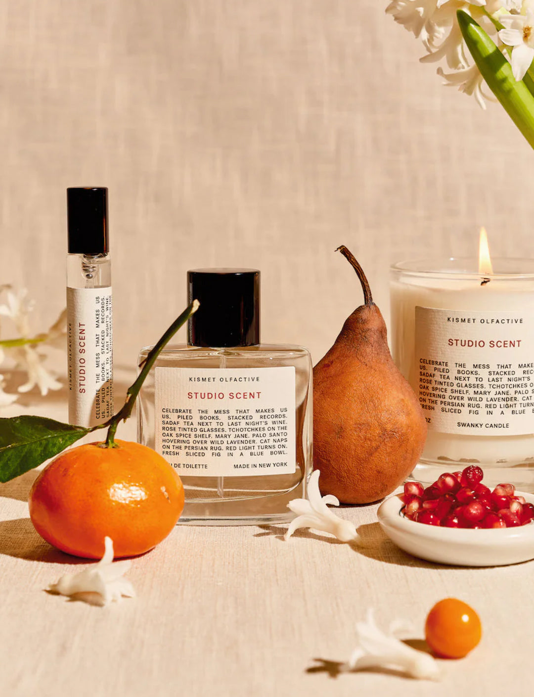 Studio Scent products including a bottle, candle, and small container on a neutral background with fruits and flowers.