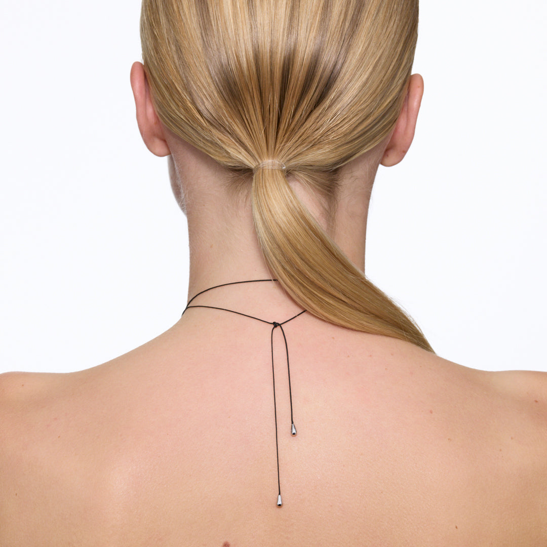 Maria Black's Tote Necklace, crafted in recycled sterling silver or 18ct gold plating features a soft trapeze-shaped pendant 'Tote' engraved with “BLACK,” it hangs from a 170cm adjustable cord made from recycled polyester.