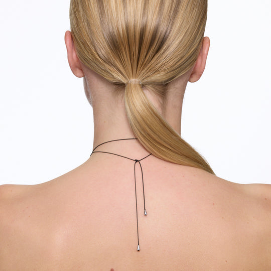 Maria Black's Tote Necklace, crafted in recycled sterling silver or 18ct gold plating features a soft trapeze-shaped pendant 'Tote' engraved with “BLACK,” it hangs from a 170cm adjustable cord made from recycled polyester.