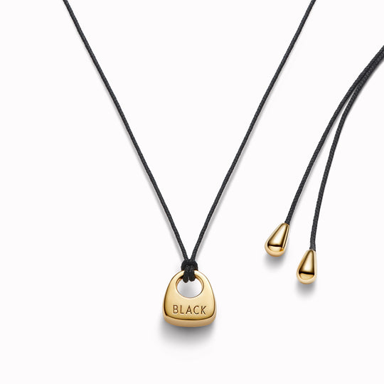 Maria Black's Tote Necklace, crafted in recycled sterling silver or 18ct gold plating features a soft trapeze-shaped pendant 'Tote' engraved with “BLACK,” it hangs from a 170cm adjustable cord made from recycled polyester