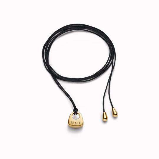 Maria Black's Tote Necklace, crafted in recycled sterling silver or 18ct gold plating features a soft trapeze-shaped pendant 'Tote' engraved with “BLACK,” it hangs from a 170cm adjustable cord made from recycled polyester