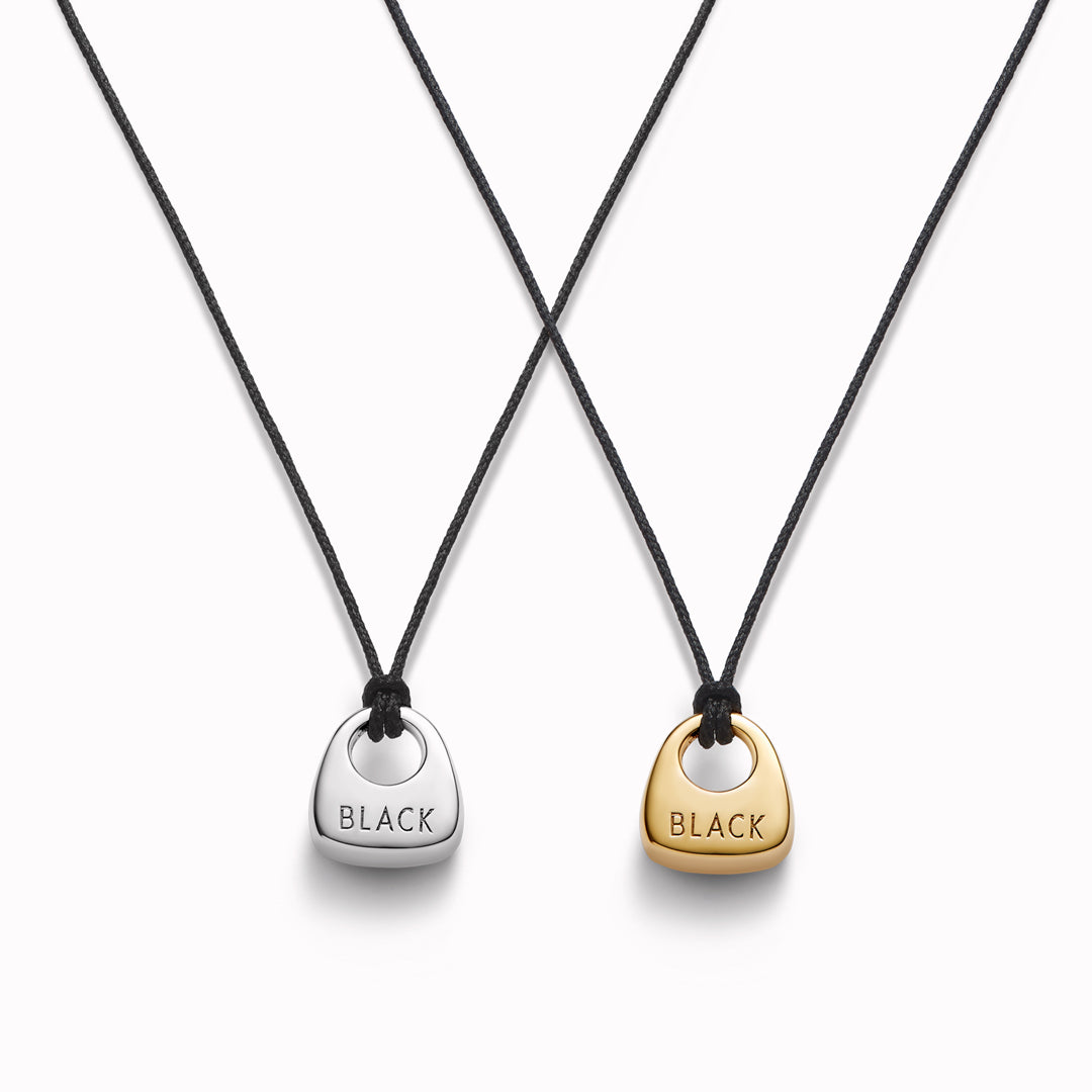 Maria Black's Tote Necklace, crafted in recycled sterling silver or 18ct gold plating features a soft trapeze-shaped pendant 'Tote' engraved with “BLACK,” it hangs from a 170cm adjustable cord made from recycled polyester