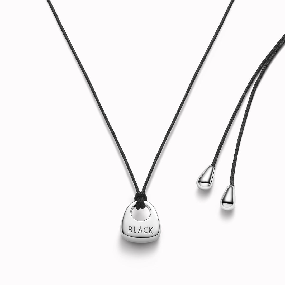 Maria Black's Tote Necklace, crafted in recycled sterling silver or 18ct gold plating features a soft trapeze-shaped pendant 'Tote' engraved with “BLACK,” it hangs from a 170cm adjustable cord made from recycled polyester.