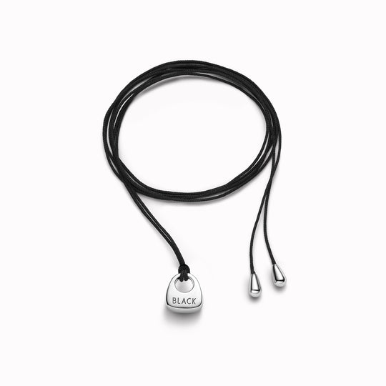 Maria Black's Tote Necklace, crafted in recycled sterling silver or 18ct gold plating features a soft trapeze-shaped pendant 'Tote' engraved with “BLACK,” it hangs from a 170cm adjustable cord made from recycled polyester.