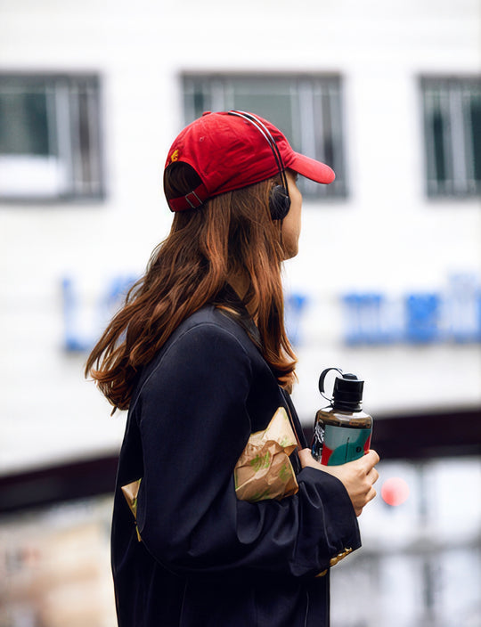 Person wearing a red cap and AIAIAI Tracks headphones, holding a water bottle and map, with a blurred background.