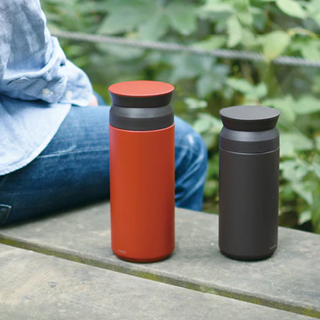 The travel tumbler by Kinto Japan is made of durable stainless steel that is easy to clean and resistant to stains and odors. It comes in various colors and sizes to suit your preferences and needs. Lifestyle shot of tumblers on bench.