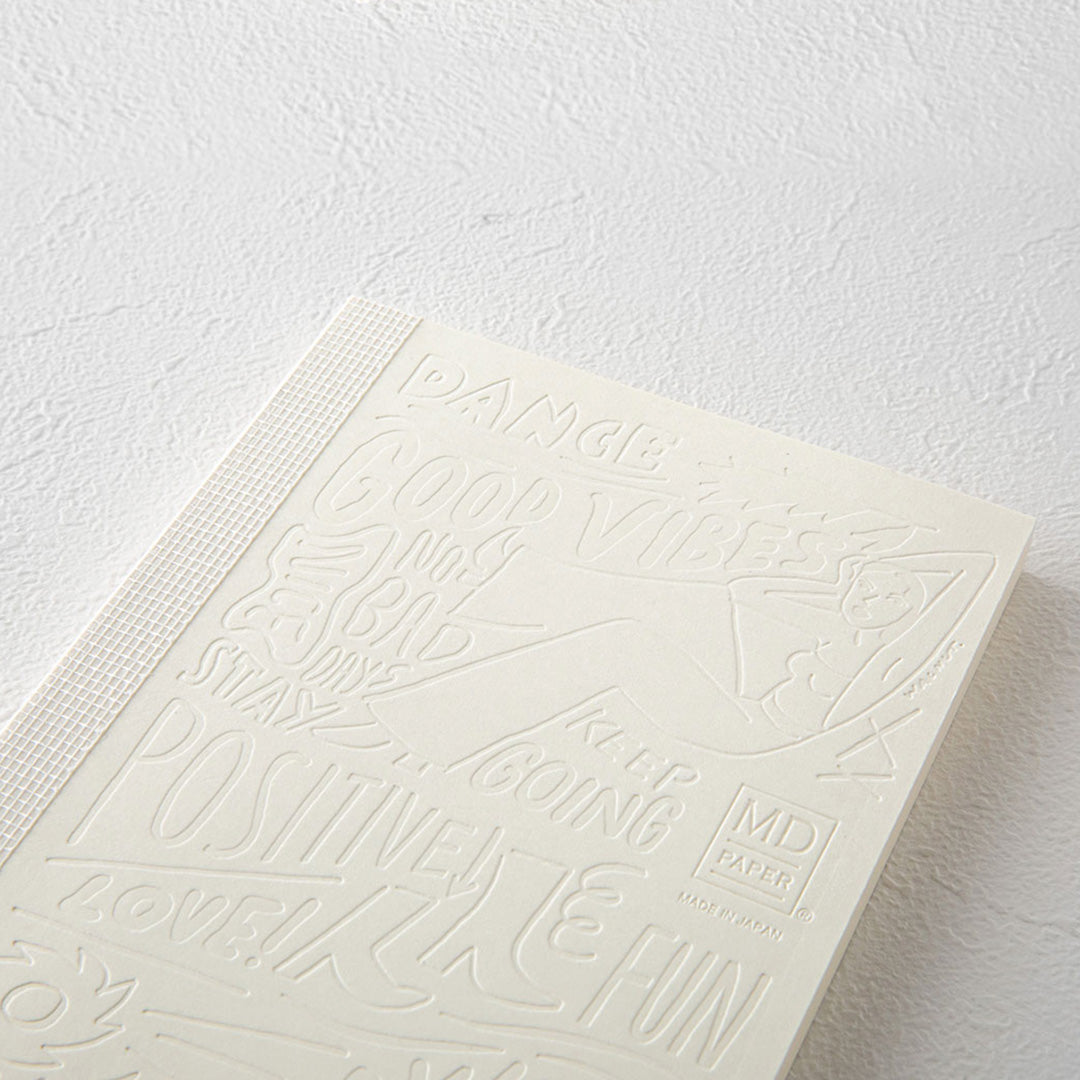 Detail of the A6 plain paper notebook that has an off white cover embossed with some ace artwork by WALNUT featuring a female figure lounging amid positive quotes such as 'Be The Sunshine'.  The MD paper logo is also emboss