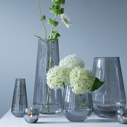 Collection of Zinc items. The Zinc Vase is a tall teardrop shaped vase made from mouth blown glass and has a pleated texture with a hand painted lustre finish. The pleated texture enhances the grey colouration that is inspired by the colour of zinc.