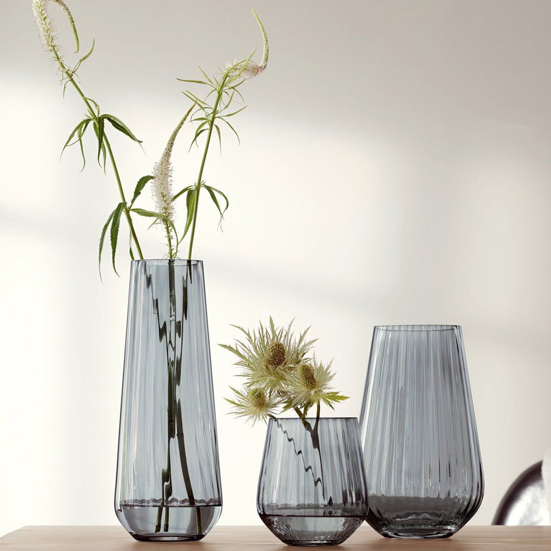Collection image on table. The Zinc Vase is a teardrop shaped vase made from mouth blown glass and has a pleated texture with a hand painted lustre finish. The pleated texture enhances the grey colouration that is inspired by the colour of zinc.