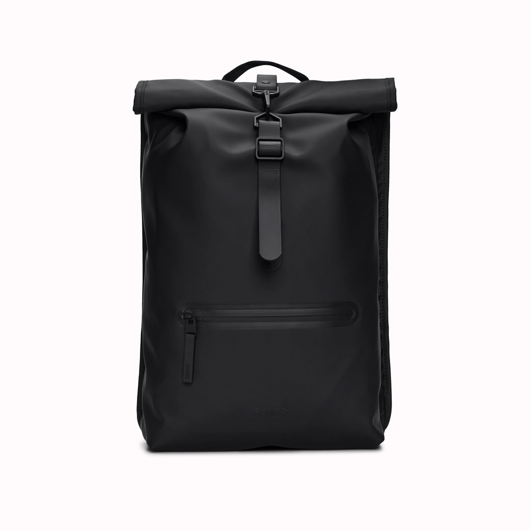 Front View of Black Rolltop Rucksack. Made from Rains’ signature waterproof fabric, this functional backpack has a roll-top closure with an adjustable strap featuring a loop for a bike lock or similar. It has a large main compartment, and an easy-access front pocket and side-access laptop compartment both with a water-repellent zipper closure. 