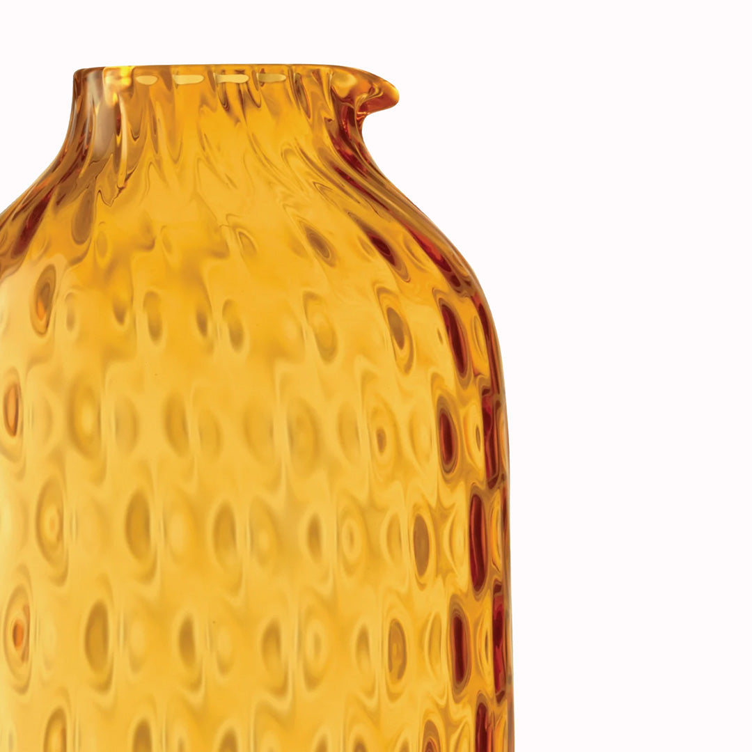 Detail, The Dapple Carafe is a lattice textured bottle shaped carafe made from coloured amber yellow mouth-blown glass. The Dapple Carafe features a beautiful undulating textured surface that is inspired by dappled sunlight on water.