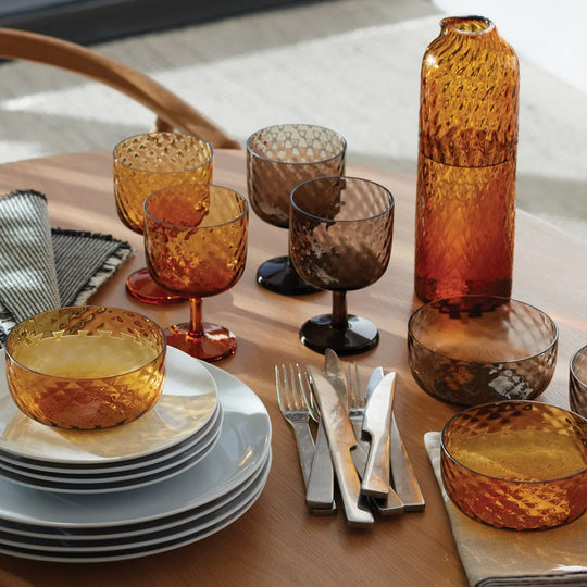 Dapple Collection. A lattice textured bottle shaped carafe made from coloured amber yellow mouth-blown glass. The Dapple Carafe features a beautiful undulating textured surface that is inspired by dappled sunlight on water.