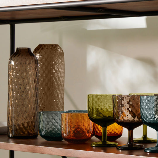 Dapple Vase is a contemporary, tall and slim shaped vase made from coloured brown mouth blown glass. The Dapple Vase features a beautiful undulating textured surface that is inspired by dappled sunlight on water.