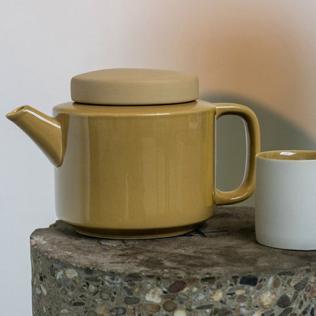 Detail of large stoneware teapot from Dutch company Kinta who produce contemporary ceramics and homeware. The large teapot is mustard yellow, with a gloss glaze exterior body finish and matt glaze lid. Its design is influenced  by ceramic trends of the 1960s, but with a pleasing modern and neutral colour palette.