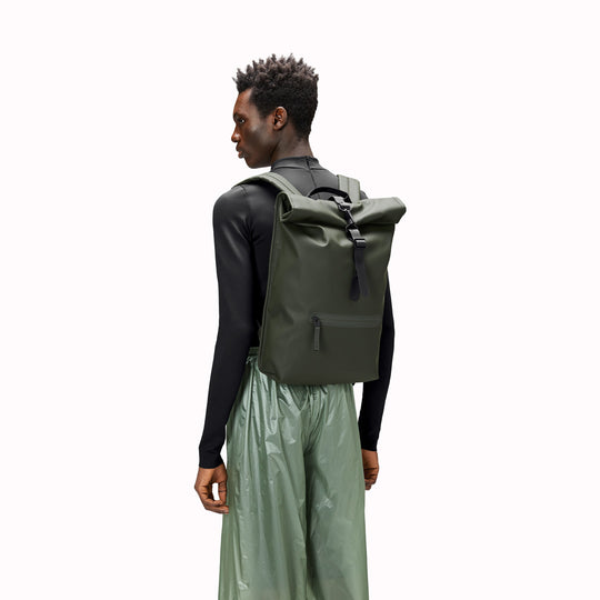 As worn by model view of Green Rolltop Rucksack. Made from Rains’ signature waterproof fabric, this functional backpack has a roll-top closure with an adjustable strap featuring a loop for a bike lock or similar. It has a large main compartment, and an easy-access front pocket and side-access laptop compartment both with a water-repellent zipper closure.
