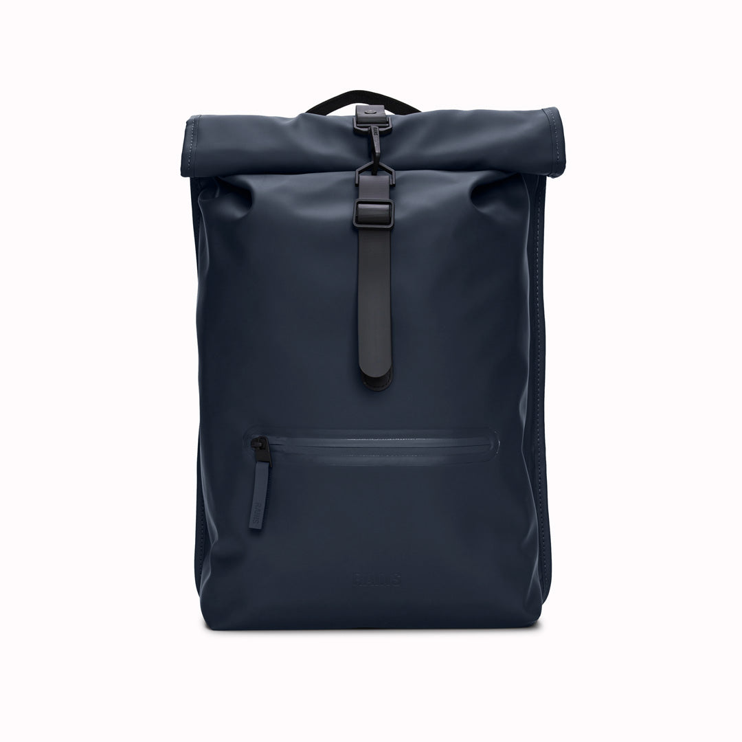 Front View of Navy Rolltop Rucksack. Made from Rains’ signature waterproof fabric, this functional backpack has a roll-top closure with an adjustable strap featuring a loop for a bike lock or similar. It has a large main compartment, and an easy-access front pocket and side-access laptop compartment both with a water-repellent zipper closure.