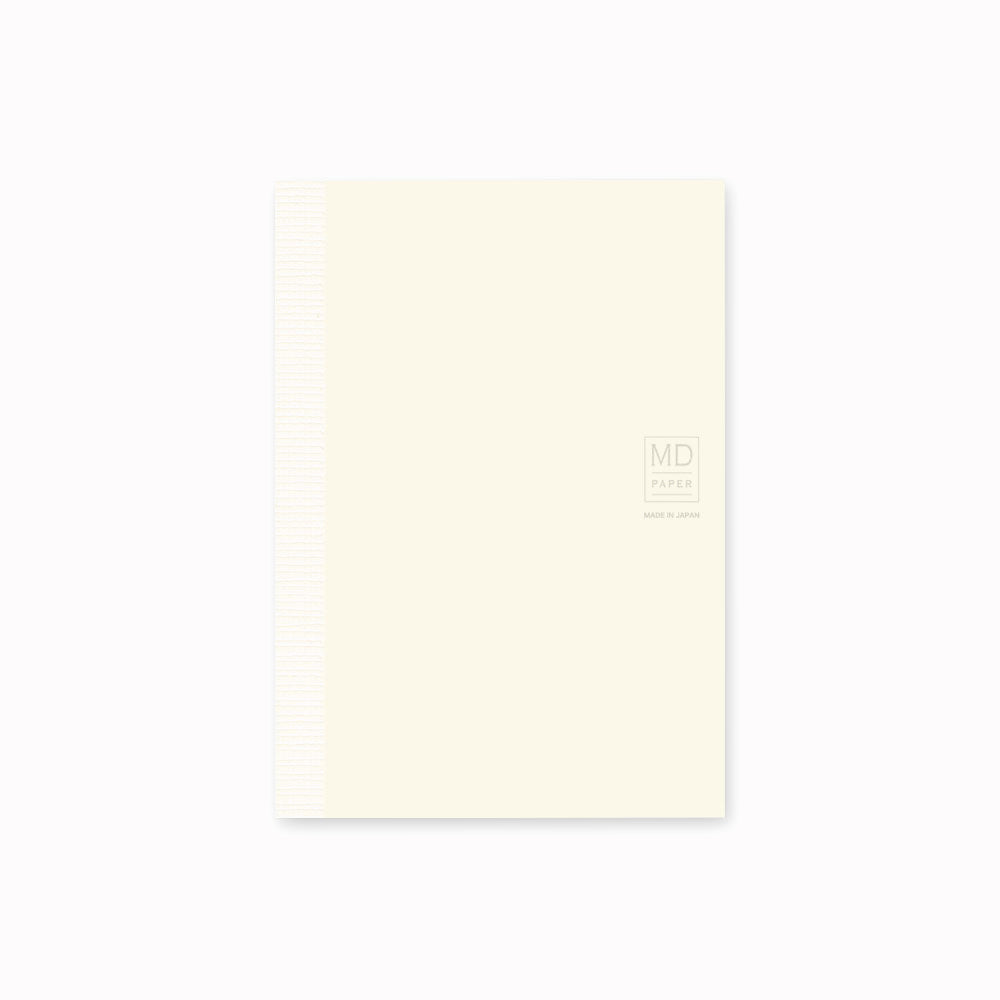 Showing notebook cover. A6 ruled paper notebook with a simple and clean off white cover and embossed MD Paper logo. MD-Paper epitomises the subtlety, elegance and simplicity of design of good Japanese stationery, concentrating on the quality of material over branding or printed design. This 176 page notebook features a ruled layout and lay-flat binding, with a paraffin paper cover for a touch of elegance.