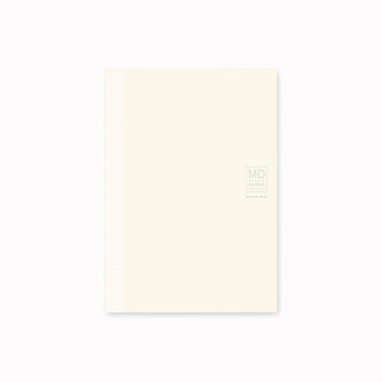 Showing notebook cover. A6 ruled paper notebook with a simple and clean off white cover and embossed MD Paper logo. MD-Paper epitomises the subtlety, elegance and simplicity of design of good Japanese stationery, concentrating on the quality of material over branding or printed design. This 176 page notebook features a ruled layout and lay-flat binding, with a paraffin paper cover for a touch of elegance.