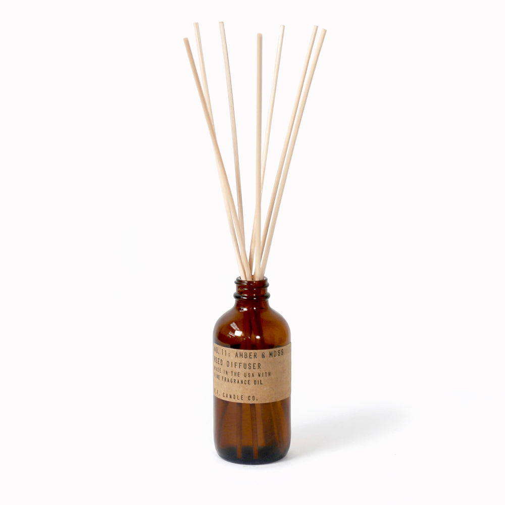 P.F. Candle Co Amber and Moss Reed Diffuser in an apothecary-inspired amber glass bottle with their signature kraft label and rattan reeds. Low-maintenance scent, all day long