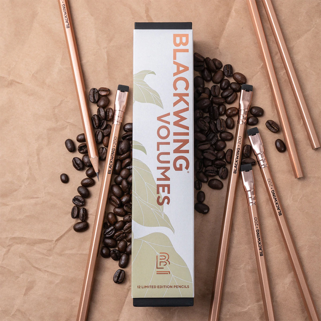 A box of Blackwing Vol. 200 pencil featuring a metallic copper design inspired by classic copper coffee roasting machines which is a tribute to the coffeehouses of the Beat Generation in NY. Pictured on a coffee bag background with coffee beans.