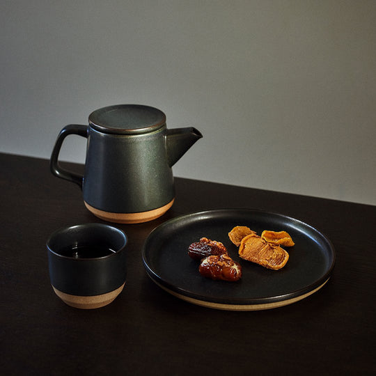 Ceramic Lab Tumbler on a table with teapot and plate. Collection from Kinto. This porcelain mug uses sandstone unique to the Hasami region in Japan. It gives the product a beautiful rough quality whilst also being delicate and a pleasure to use.