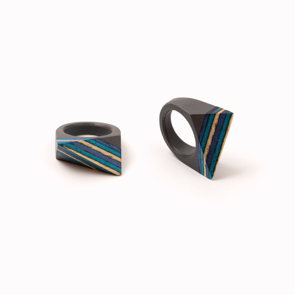 Handmade Skateboard rings by contemporary jewellery designer Simone Frabboni. The base of the ring is made of resin, the top of recycled skateboard decks. Dark grey statement ring with multi colour blue striped top