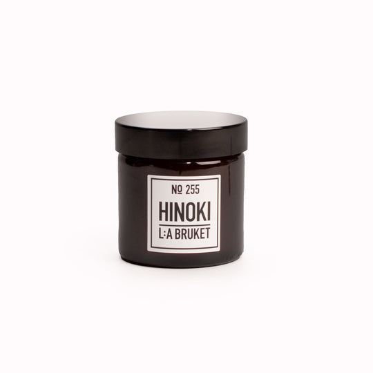 Hinoki Travel Sized Scented Candle with Lid from L:A Bruket. Hinoki scented travel candle from L:A Bruket, made of wax from organic soy with a burn time of more than 15 hours. The candle is filled by hand in a mouth-blown amber tinted glass.