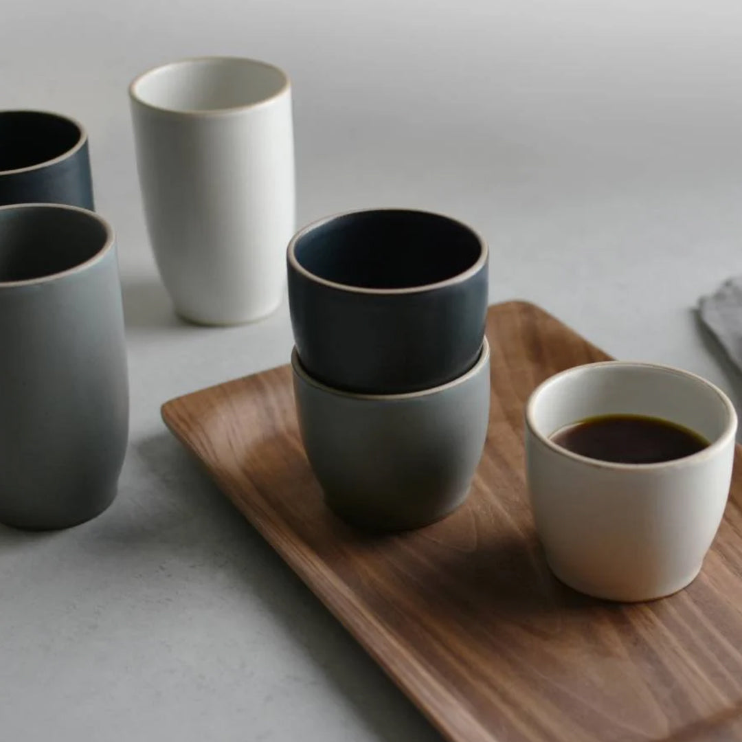 Lifestyle shot, Nori Tumblers. The 350ml Black Nori Porcelain Tumbler  is a Japanese manufactured tall black tea, coffee or juice cup from Kinto. The porcelain has a tactile sloping side and smooth finish which feels pleasing in your hands. The glaze is a tasteful matt black stone with raw porcelain edges in the Japanese style. 