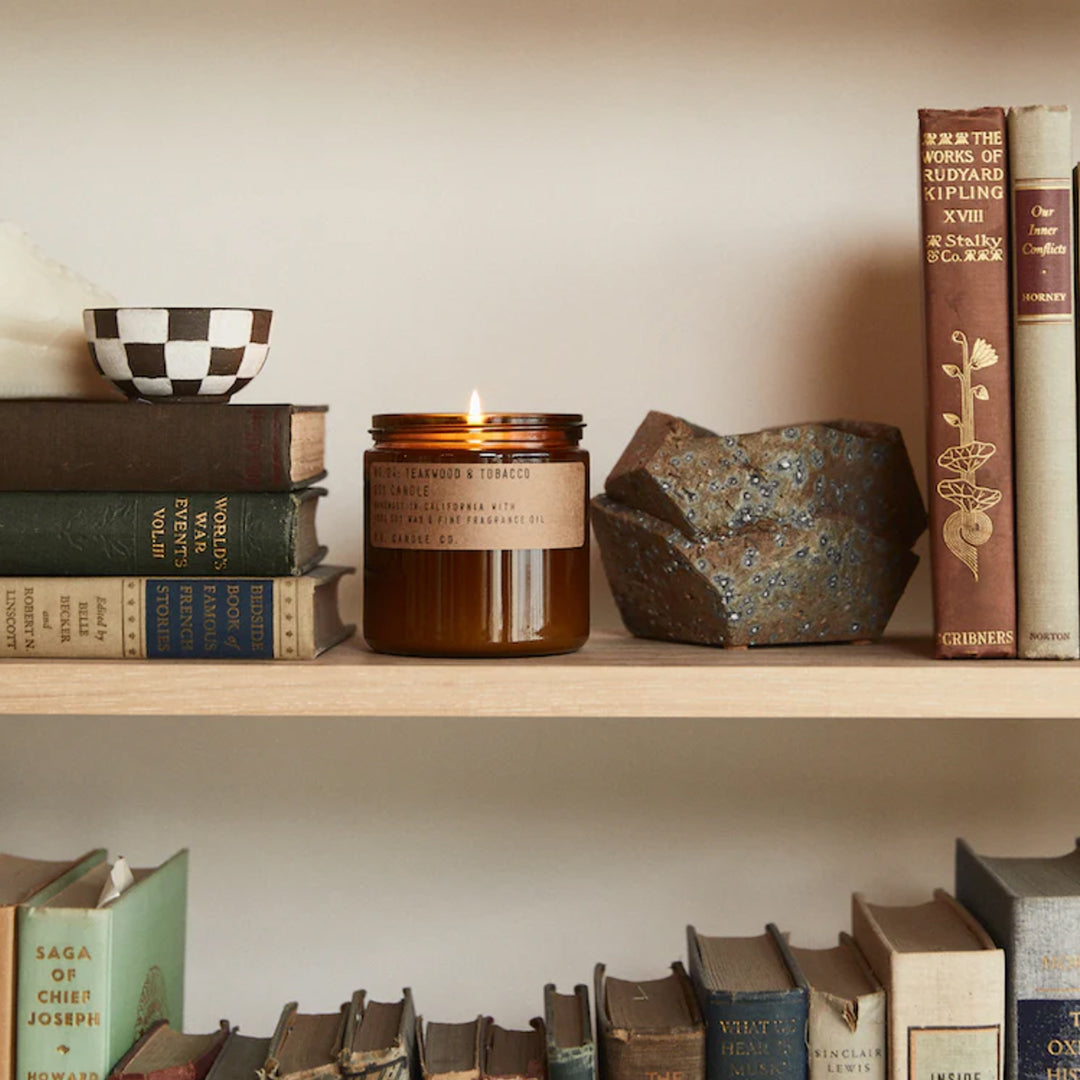Teakwood and Tobacco Fragranced Soy Large Candle in classic amber jar on a bookshelf