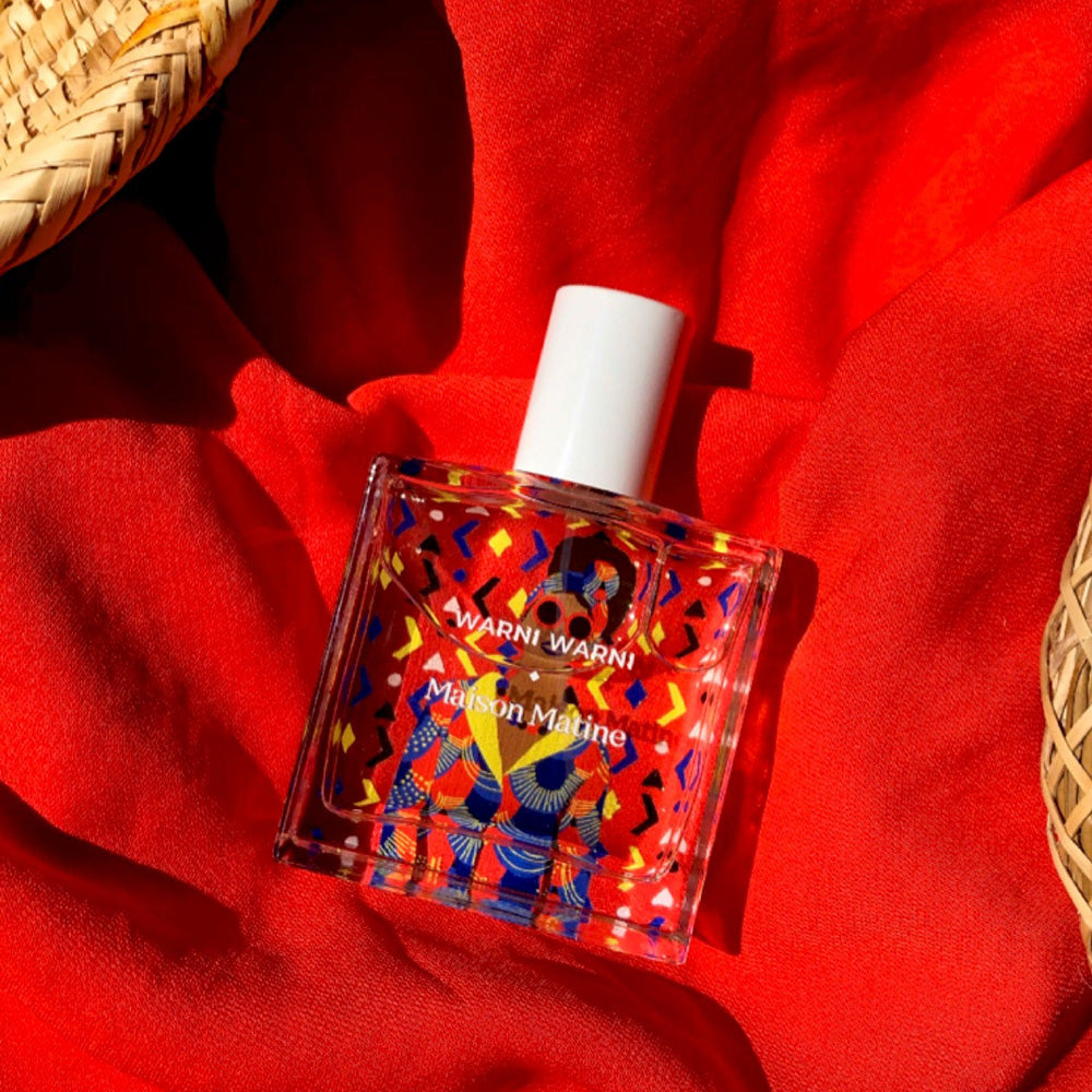Maison Matine's 'Warni Warni' is a scent inspired by a sharing, welcoming diversity and cultural mixing, all housed in an illustrative glass bottle. The name means 'come to me' which is an invitation to share in Arabic. Patterned 50ml bottle with woman in sunglasses, on red fabric