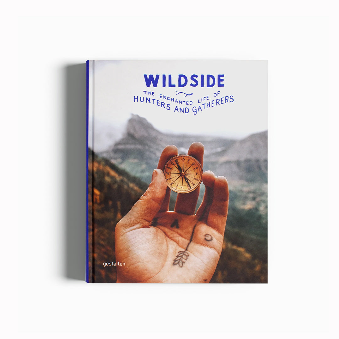 Wildside- The Enchanted Life of Hunters and Gatherers book, cover. Compass in hand, mountains in background. The Enchanted Life of Hunters and Gatherers. Retreat into nature, meet mushroom pickers, collectors, and explorers; build cabins and scenic trails, create crafts, or start inspired projects with this book. This is the way to the forest.